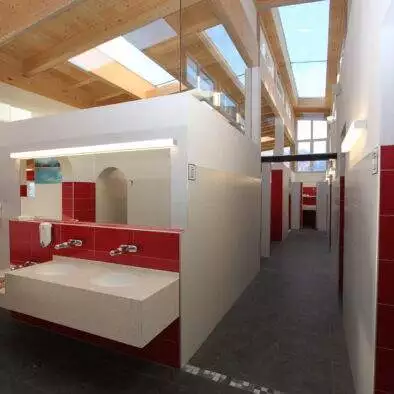 Sanitäranlage weiß mit beleuchtetem Spiegel und roten Akzentfliesen. Ein Kleinkind wäscht sich gerade die Hände.